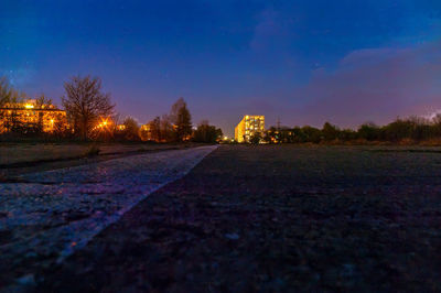 Illuminated road by field against sky at night