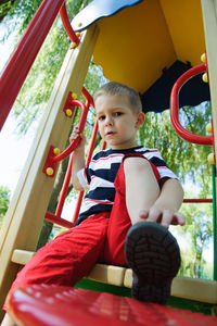 Cute boy sitting on slide in playground
