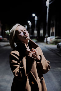 Young woman with umbrella on road in city at night