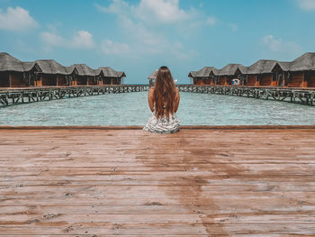 Rear view of woman sitting on pier at sea against sky