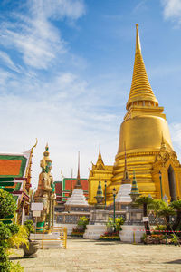 A demon guardian statue with a great golden stupa in wat phra kaew against the sky