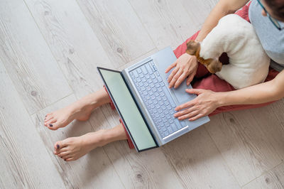 High angle view of woman using laptop while sitting with dog on floor