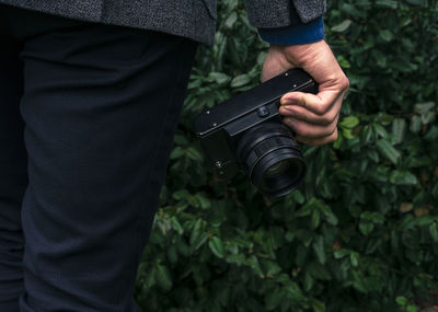 Midsection of man holding camera against plants