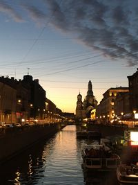 River amidst illuminated buildings against sky at sunset