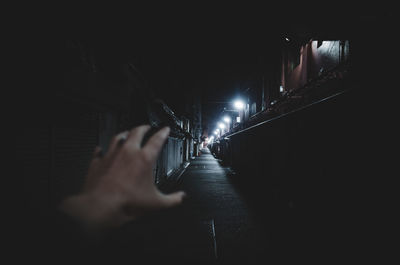 Cropped hand of woman gesturing at alley during night