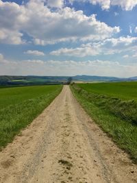 Dirt road amidst agricultural field against sky