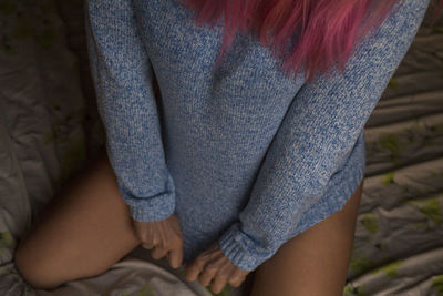 Midsection of young woman kneeling on bed at home