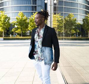 Determined black male wearing fancy clothes walking along glass building in city and looking away