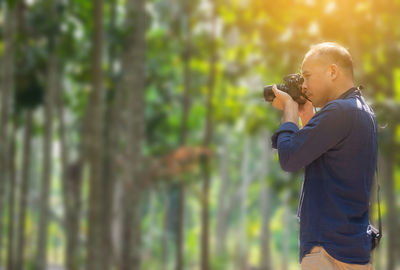 Side view of man holding camera while standing on land