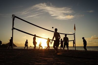People playing volleyball at beach against sky during sunset
