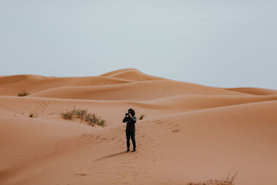 Full length of man photographing while standing on sand in desert against sky