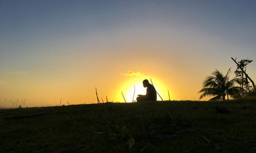 Silhouette man on field against sky during sunset