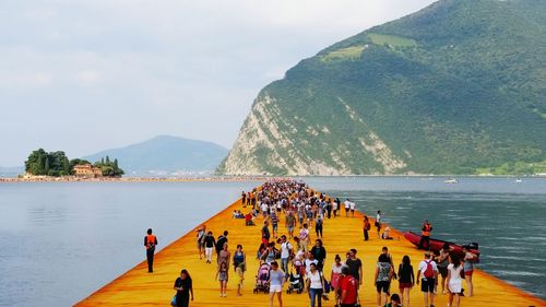 People on pier over river against mountain