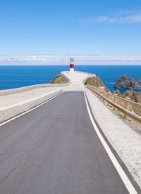 Road leading towards lighthouse by sea against sky