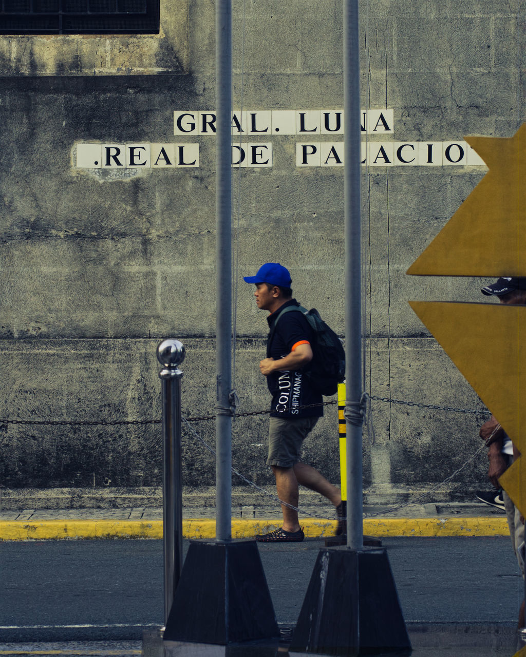 full length, one person, architecture, road, street, text, communication, infrastructure, men, yellow, city, sign, blue, lifestyles, day, western script, built structure, transportation, urban area, side view, wall, person, outdoors, adult, building exterior, leisure activity, wall - building feature, clothing, art