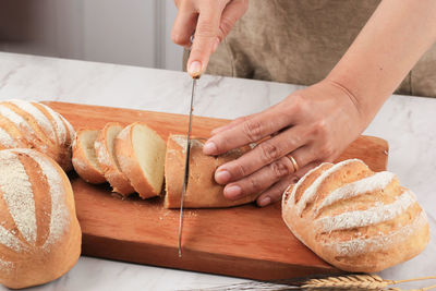 Female hands cutting wheat white bread on the wooden board, selective focus