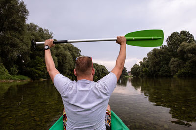 Rear view of man holding boat in lake against sky