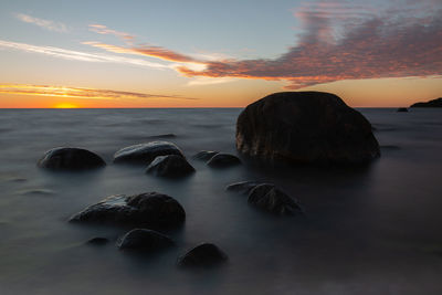 Rocks on beach against sky during sunset