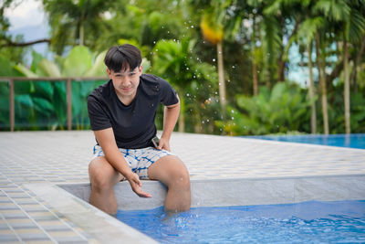 A young adult asian male model sitting alone relax at the swimming pool.one person portrait.