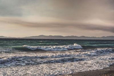 Waves rushing towards shore against sky during sunset