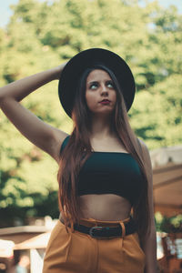 Young adult woman standing and holding her black hat while looking up