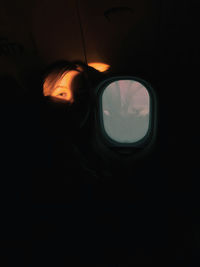 Cropped image of silhouette of woman in airplane at sunset