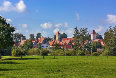 Trees and houses on field against sky