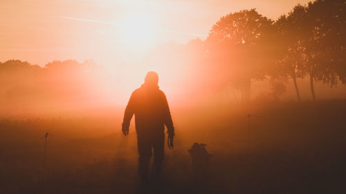 Silhouette teenager boy with dog against sky during sunset