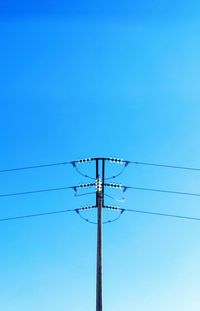 Low angle view of electricity pylon against clear blue sky