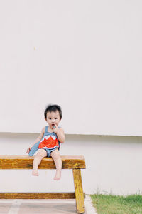 Portrait of cute girl sitting on chair against wall
