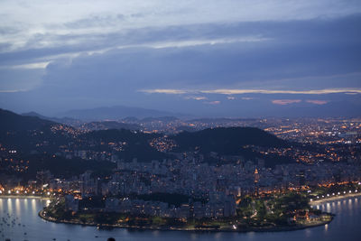 Illuminated city by sea against sky