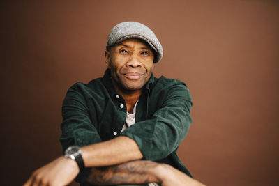 Portrait of mature man wearing beret over brown background in studio