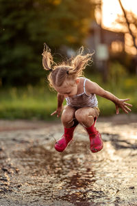 Child jumping through puddles in red rubber boots