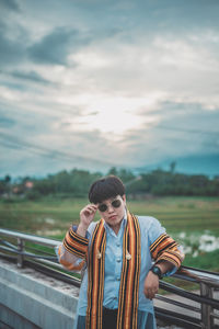 Portrait of man standing by railing against sky