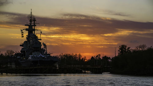 Silhouette of temple by river against sky during sunset