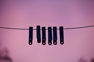 Low angle view of silhouette clothespins hanging on clothesline during sunset