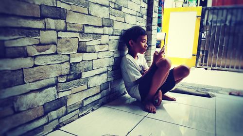 Side view of young woman sitting against brick wall