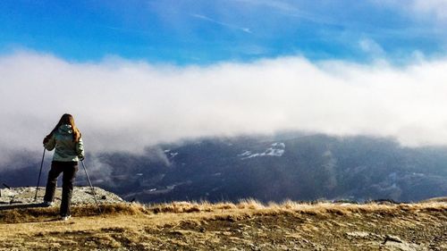 Full length rear view of woman standing on mountain against cloudy sky