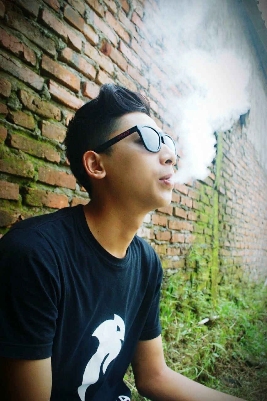 YOUNG MAN LOOKING AWAY AGAINST BRICK WALL