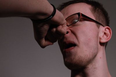 Cropped image of hand punching man against gray background