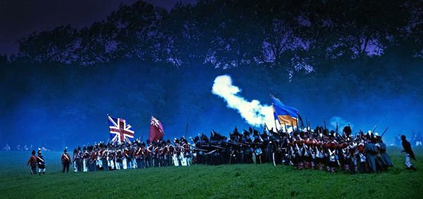 Crowd with flags for war standing on grassy field against mountains