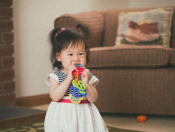 Cute girl biting toy while standing at home