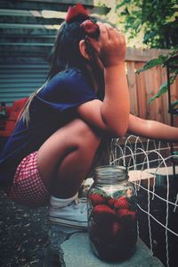 Girl crouching by jar of strawberries on retaining wall