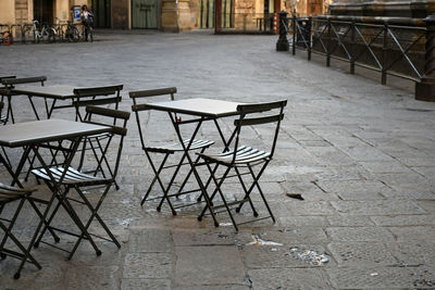 Empty chairs and tables at sidewalk cafe by building