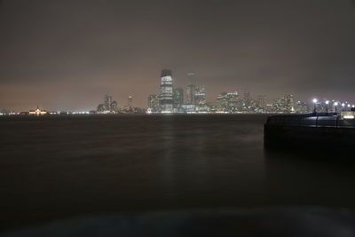 Illuminated buildings by sea against sky at night