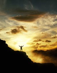 Low angle view of silhouette person with arms outstretched standing against sky during sunset