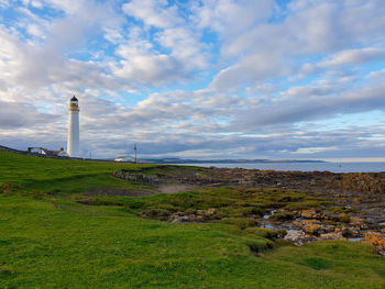 Lighthouse on field by buildings against sky