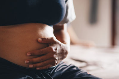 Midsection of pregnant woman sitting with hands on stomach at home