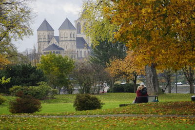 Woman sitting in park against buildings during autumn