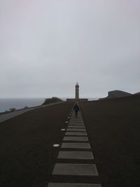 Distant person on desolate volcanic landscape walks away in lighter stepstone to faraway lighthouse